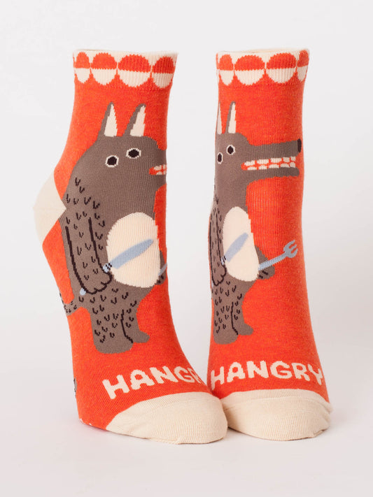 Blue Q's Hangry W-Ankle Socks feature two orange combed cotton ankle socks with a cartoon wolf holding a fork and knife, “HANGRY” in white on the toes, and a playful hungry expression for extra fun.