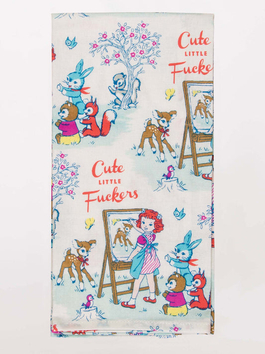 The Blue Q Cute Little Fuckers Dish Towel features vintage-style art of animals and a girl painting, with “Cute Little Fuckers” in red cursive repeated across the fabric.
