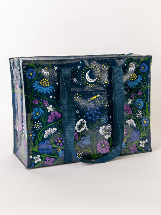 The Blue Q Starry Garden Shoulder Tote is a reusable, spacious bag with dark blue handles, featuring colorful floral patterns and night sky accents—crescent moon, stars, and a shooting star—on a glossy navy background for stylish shopping.