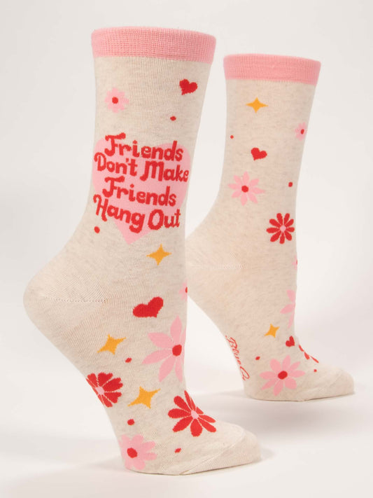 The Blue Q Friends Don't Make Friends Hang Out W-Crew Socks are beige combed cotton with pink cuffs, featuring red, pink, and yellow flowers and hearts. The socks display the text: Friends don't make friends hang out.