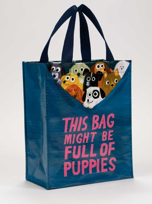 The Blue Q "This Bag Might Be Full Of Puppies Handy Tote" is a blue reusable bag with dark blue handles, pink text, and cute cartoon puppy faces peeking out—perfect for puppy lovers on the go.