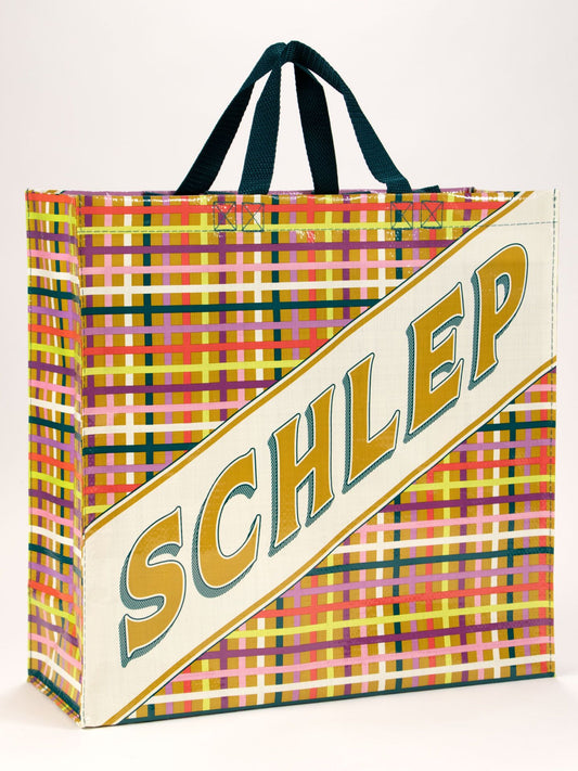 The Schlep Shopper by Blue Q is a colorful checkered tote featuring two dark handles and "SCHLEP" in large yellow letters across a white panel—a standout bag for everyday use.
