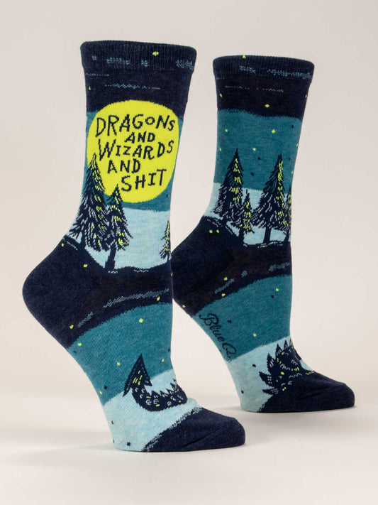 Two blue Blue Q crew socks with a nighttime forest scene featuring green trees, fantastical creatures, and a dragon silhouette. One sock has “Dragons And Wizards And Shit” inside a yellow moon.