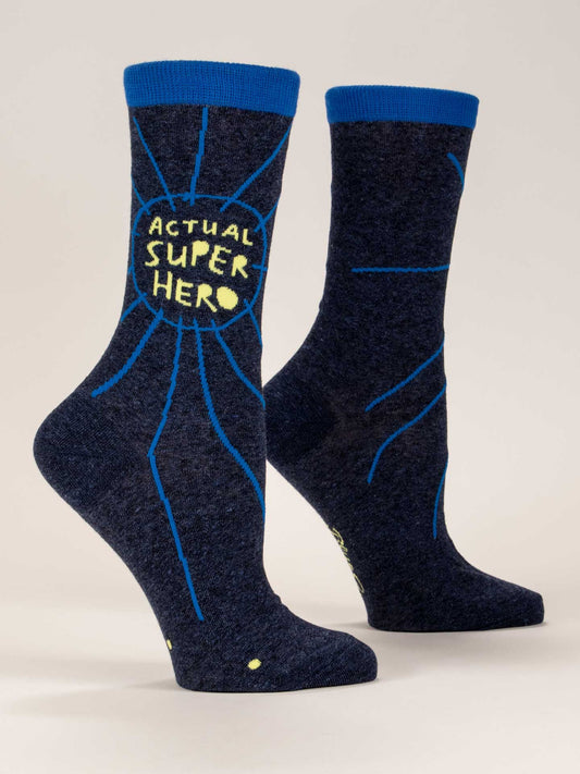 Blue Q Actual Superhero W-Crew Socks: two navy blue combed cotton socks with blue cuffs, spiderweb designs, and "ACTUAL SUPER HERO" in yellow on the sides, reinforced with a nylon-spandex blend, displayed upright against a plain background.
