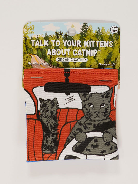 The Blue Q Talk To Your Kittens About Catnip Toy is a cotton pouch for cats with two gray cats in a red car and the phrase TALK TO YOUR KITTENS ABOUT CATNIP™. Features organic catnip, plus trees and blue sky in the background.
