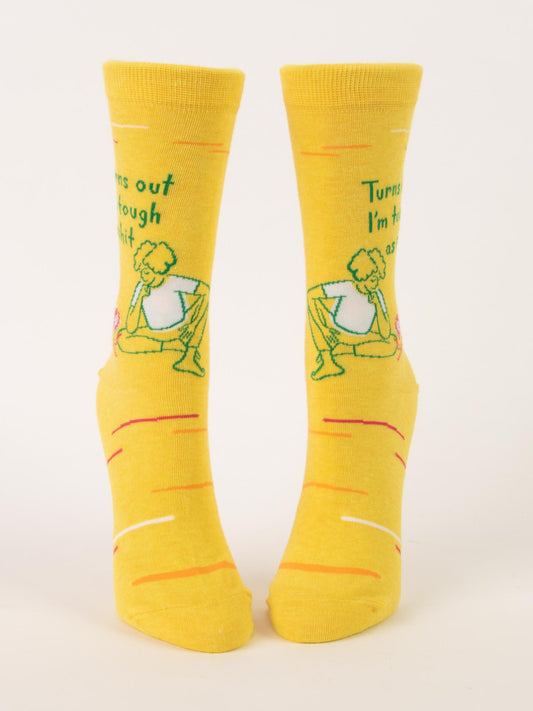 Blue Q Turns Out I'm Tough As Shit W-Crew Socks are bright yellow, made from soft combed cotton. They feature a cartoon weightlifter, bold text saying "Turns out I’m tough as shit," plus scattered red and white lines.