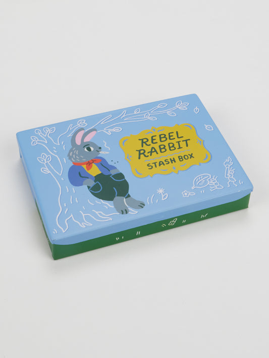 A rectangular box labeled “Rebel Rabbit Pocket Box” by Blue Q features an illustrated rebel rabbit with fuzzy paws in a blue jacket sitting by a tree, set against a blue and green background with white decorative accents.