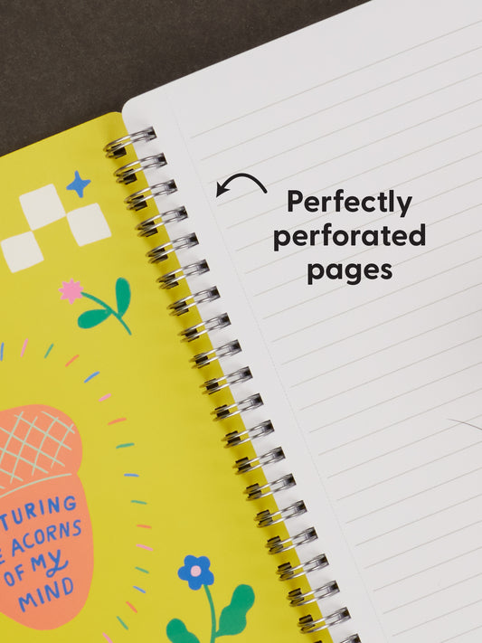 Open Blue Q’s Random Crap 6x8 Spiral Notebook with a yellow illustrated cover on the left and lined, perforated white pages on the right. An arrow points to the pages with the caption: Perfectly perforated pages for stashing your acorns of wisdom—even in lean times.