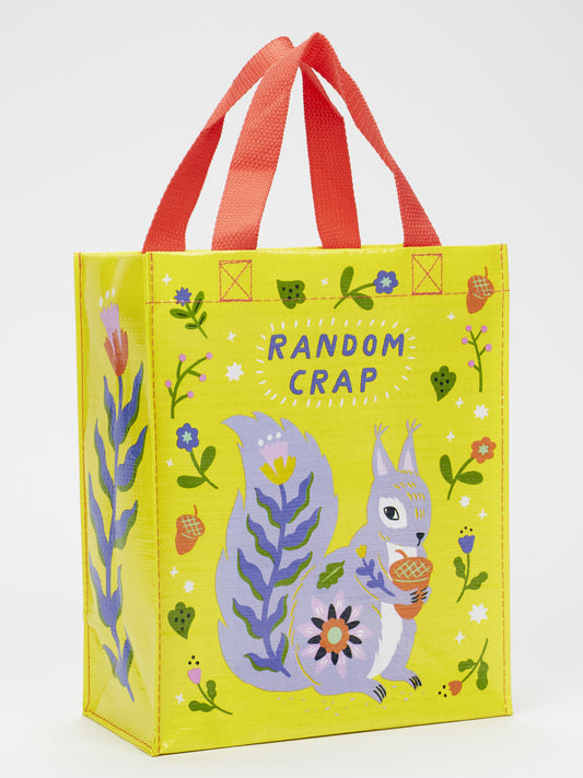 The Blue Q Random Crap Handy Tote is a yellow reusable bag made from recycled material with red handles, showing a purple squirrel with an acorn among flowers and acorns. "RANDOM CRAP" is written above—great for quirky storage or organization.