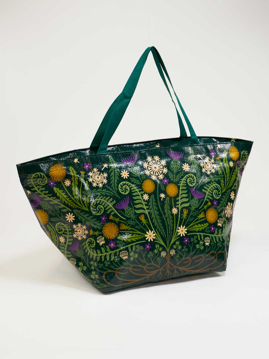 The Wild Bloom Big Bag by Blue Q is a spacious recycled travel tote with dark green handles, featuring a vibrant glossy floral and foliage print in yellow, white, and purple.