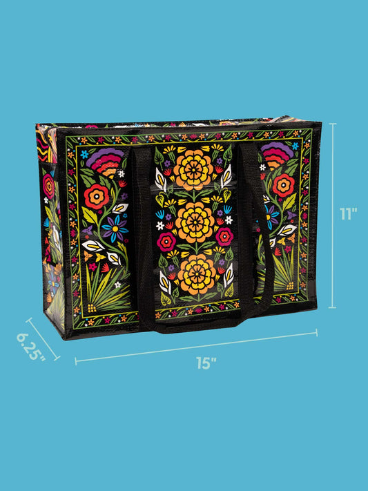 The Blue Q Flower Fest Shoulder Tote features festive red, yellow, orange, and green floral designs on black. Both functional and stylish, it measures 15"W x 11"H x 6.25"D and is shown on a blue background.