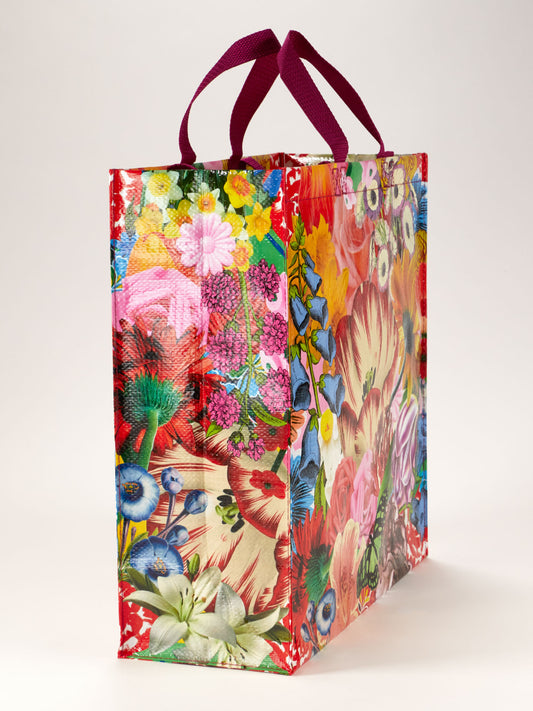 The Blue Q Blossom Shopper is a colorful, rectangular reusable bag with a vibrant floral POWER flower design and dark pink handles, shown standing upright on a neutral background.