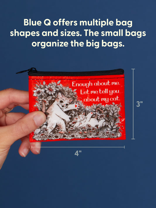 A hand holds the Blue Q “Enough About Me. Let Me Tell You About My Cat.” Coin Purse—a red 4x3 zippered pouch featuring a charming cat illustration and quirky text, perfect for sparking conversation or celebrating your love of cats. Blue Q offers this coin purse along with other bag shapes and sizes.