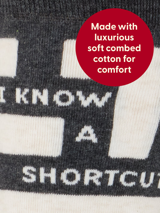 Close-up of Blue Q’s I Know A Shortcut M-Crew Socks in black and white, featuring the text “I KNOW A SHORTC...” and a red circle overlay stating, “Made with luxurious soft combed cotton and a hint of spandex for comfort.”.