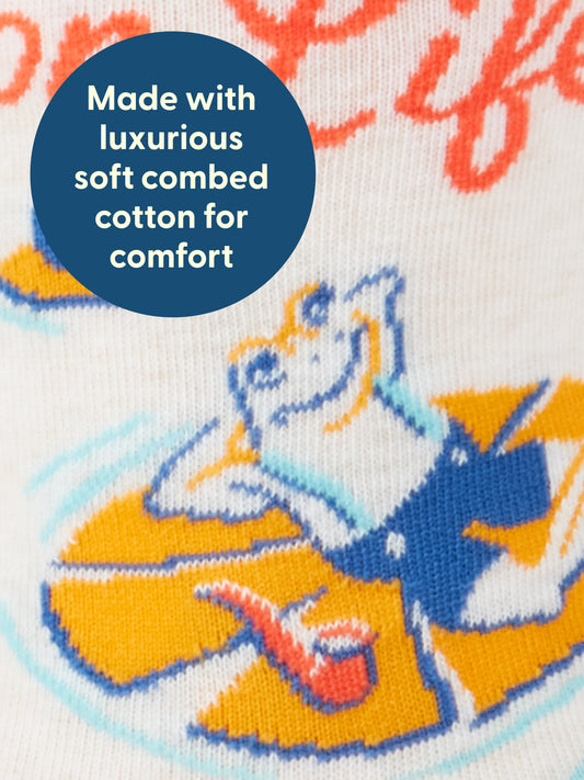 Close-up of fabric featuring a cartoon frog lounging on a yellow float. Blue circle overlay reads, Made with luxurious soft combed cotton for comfort. These playful High On Life...And Possibly Weed M-Crew Socks by Blue Q are crafted from combed cotton and designed to fit men's shoe size 7-12, ensuring both style and an exceptional fit.