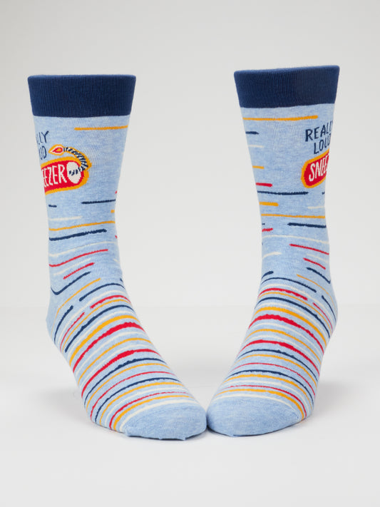 A pair of Blue Q Really Loud Sneezer M-Crew Socks in blue cotton, featuring multicolored horizontal stripes, navy blue cuffs, and a patch reading “REALLY LOUD SNEEZER” on the sides. Designed to fit men’s shoe size 7-12.