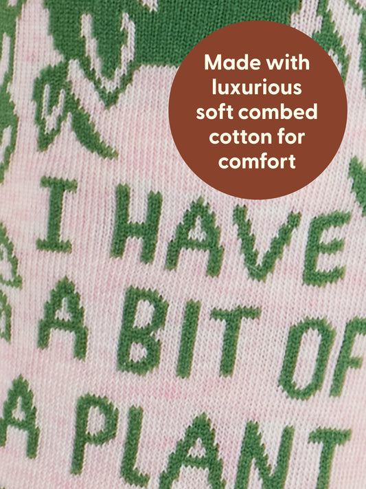 Close-up of Blue Q’s “I Have A Bit Of A Plant Problem” W-Crew Socks: pink and green knit with monstera leaves, text on front, a round brown “luxurious soft combed cotton” label. Fits women’s shoe size 5-10.