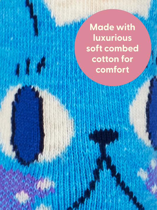 Close-up of blue knitted fabric featuring a charming cartoon cat face, with a pink circle overlay text: Made with luxurious soft combed cotton for ultimate comfort. The Cuddle Me Bitch W-Crew Socks by Blue Q bring together playful novelty style and the unbeatable softness of combed cotton.