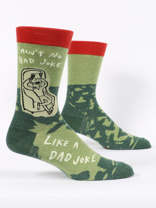Blue Q Ain't No Bad Joke Like A Dad Joke M-Crew Socks feature a green camo pattern, red cuffs, and a cartoon man relaxing in a chair with the quote: "Ain't no bad joke like a dad joke." Made from soft combed cotton.