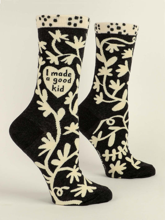Blue Q’s I Made A Good Kid W-Crew Socks feature black combed cotton, cream floral patterns, and a heart with "I made a good kid" on one sock. Photographed on a plain neutral background.
