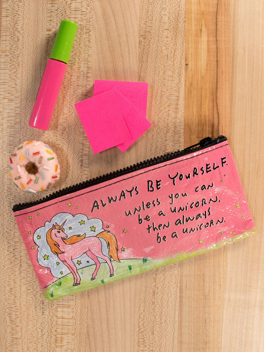 The Blue Q "Always Be Yourself Unless You Can Be A Unicorn" Pencil Case features a pink unicorn design and inspiring message, seen here on a wooden surface with a pink marker, sticky notes, and a mini donut.