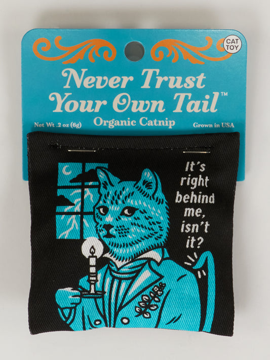 The Blue Q Never Trust Your Own Tail Catnip Toy package shows a cat in Victorian clothing holding a candle with the phrase "It’s right behind me, isn’t it?" and promotes healthy play with organic catnip.