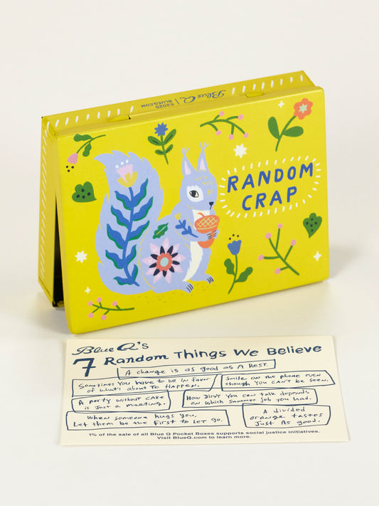 The Blue Q Random Crap Pocket Box is a yellow storage box with an illustrated blue squirrel holding an acorn, labeled "Random Crap." It’s shown behind a white card, making it perfect for storing small items.