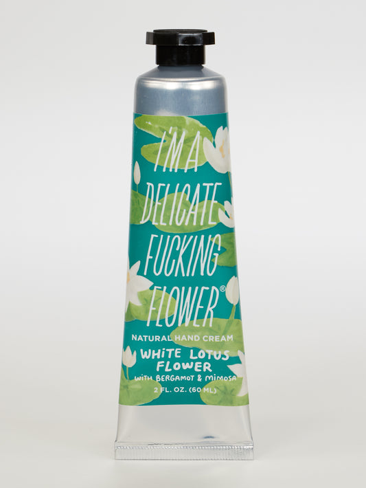 A green floral tube of Blue Q's I'm A Delicate Fucking Flower Natural Hand Cream—White Lotus Flower with Bergamot & Mimosa—features white lotus illustrations.