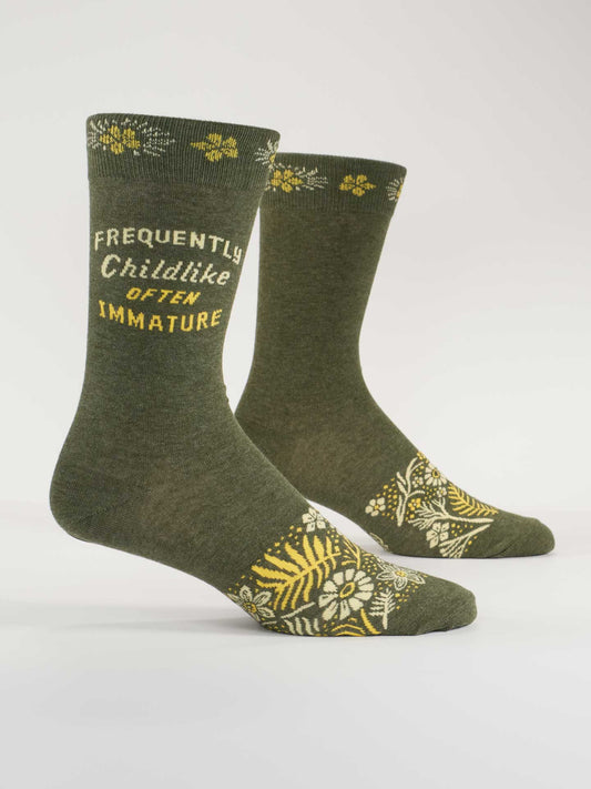 Blue Q’s Frequently Childlike Often Immature M-Crew Socks are green combed cotton with yellow and white floral patterns and playful text—ideal for anyone who’s faced silly nicknames or surprise wedgies.