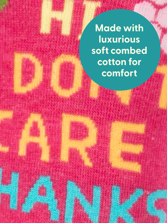 A close-up of Hi, I Don't Care, Thanks W-Crew Socks by Blue Q shows pink fabric with yellow and teal text and a teal circle stating they’re made with luxurious soft combed cotton for comfort—perfect women’s socks.
