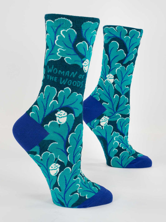 Blue Q's Woman Of The Woods W-Crew Socks are blue and teal women's socks featuring leafy patterns and "Woman of the Woods" text, shown on mannequin feet against a white background—ideal cotton socks for nature lovers.